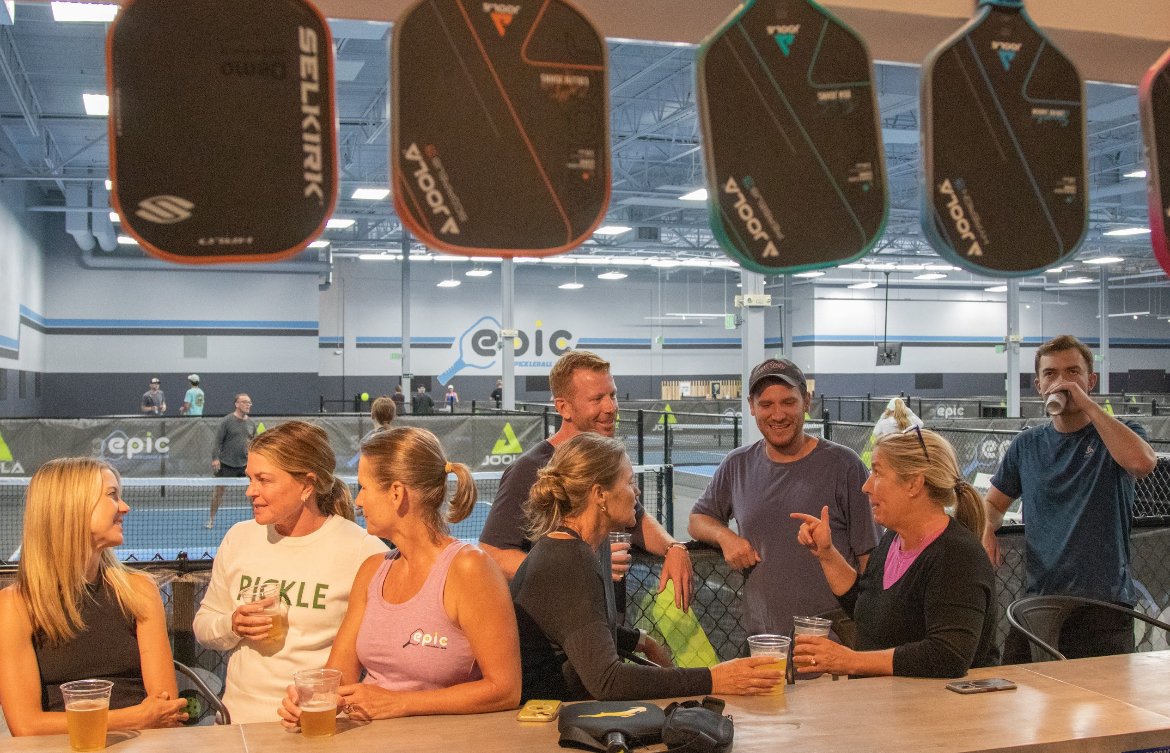 Members gathered at the bar under hanging paddles at Epic Pickleball Club