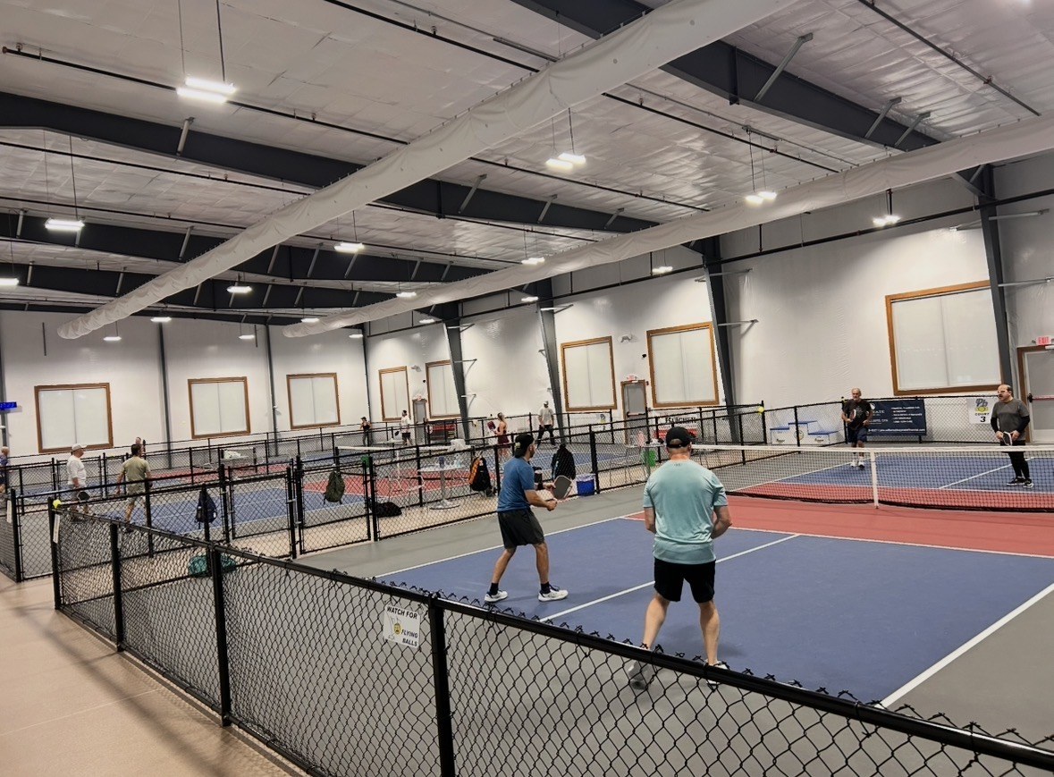 Indoor championship courts separated by four-foot fencing and a center walkway at Pickleball 603