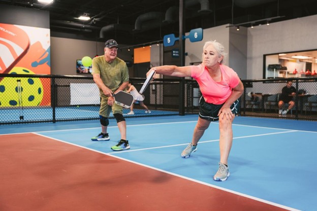 Two older pickleball players reaching for a shot on an indoor club court